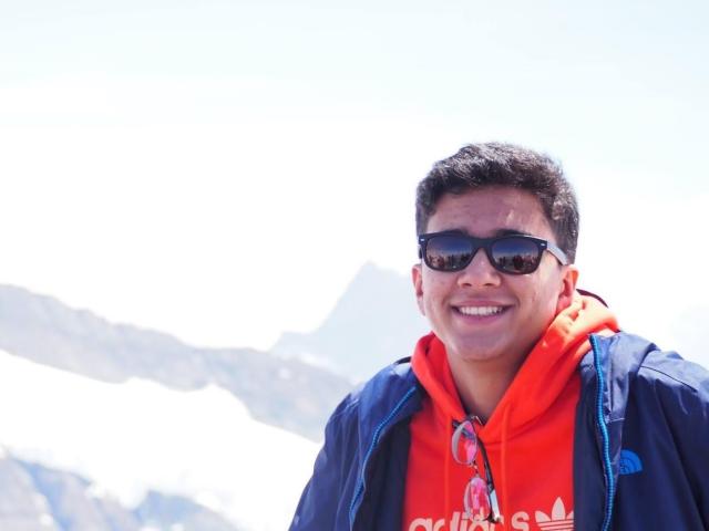 Jaskaran smiling with sunglasses and a snowy mountain top in the background.
