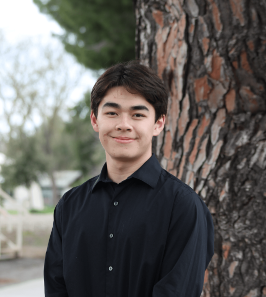 Young man in a black shirt stands by a tree, looking joyful.