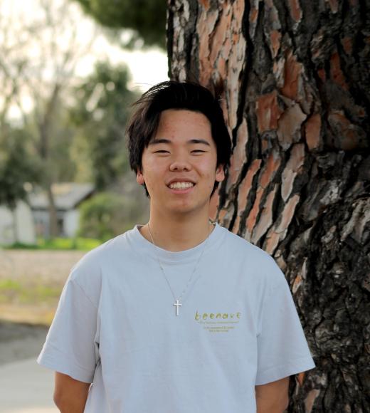Joyful and smiling man, white T-shirt, standing by a tree.