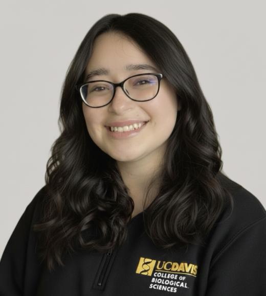 Young woman with long, dark hair and glasses, smiling in a black sweatshirt on a light background.