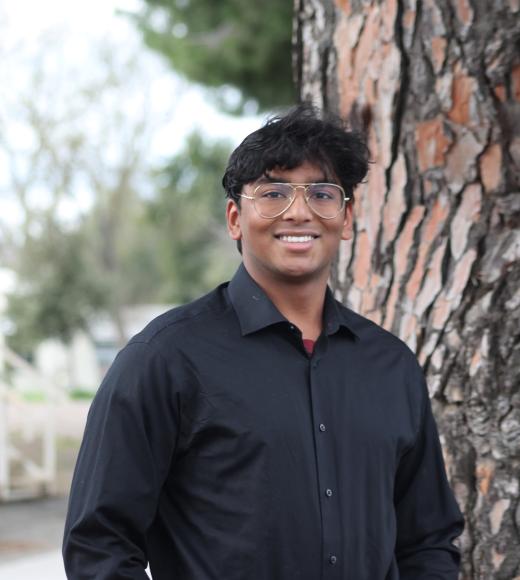 Young man in a black shirt stands by a tree, looking joyful.