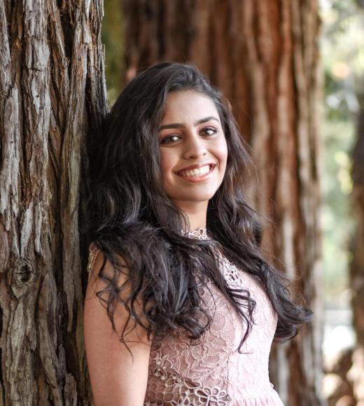 Neha smiling against a redwood tree trunk