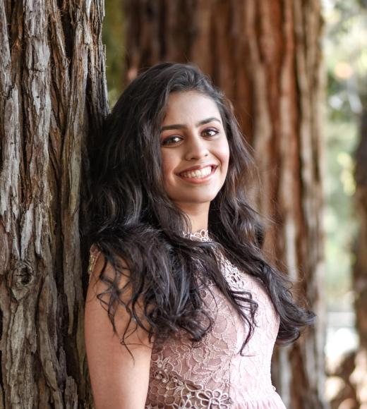 Neha smiling against a redwood tree trunk