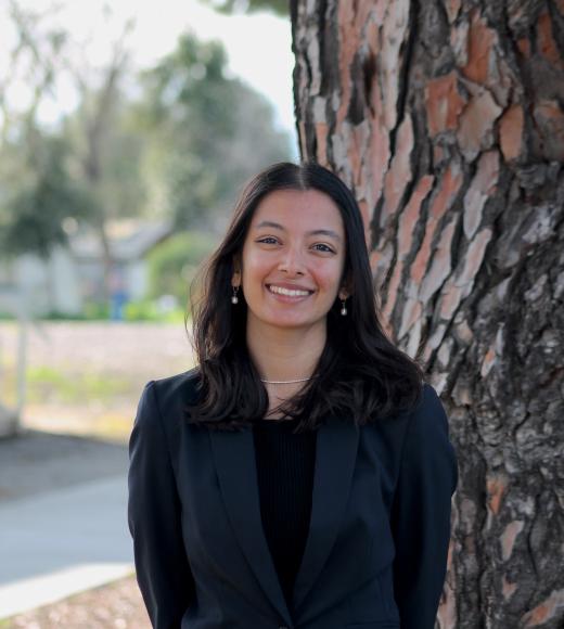 Young woman in a black sweater stands by a tree, looking joyful.