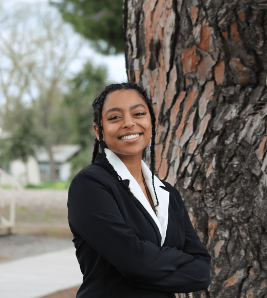 Young woman in a black sweater stands by a tree, looking joyful.