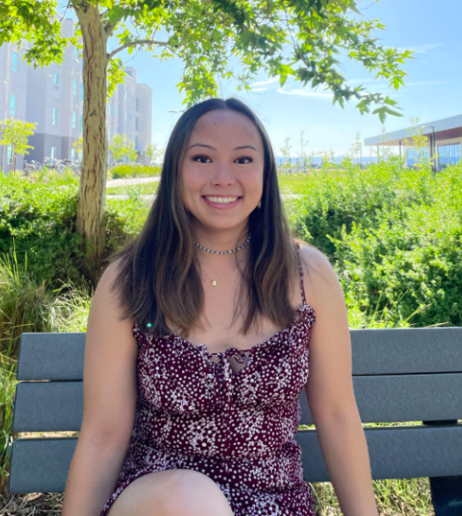 Sara is smiling on a bench with a grass background