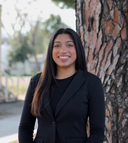 Young woman in a black sweater stands by a tree, looking joyful.
