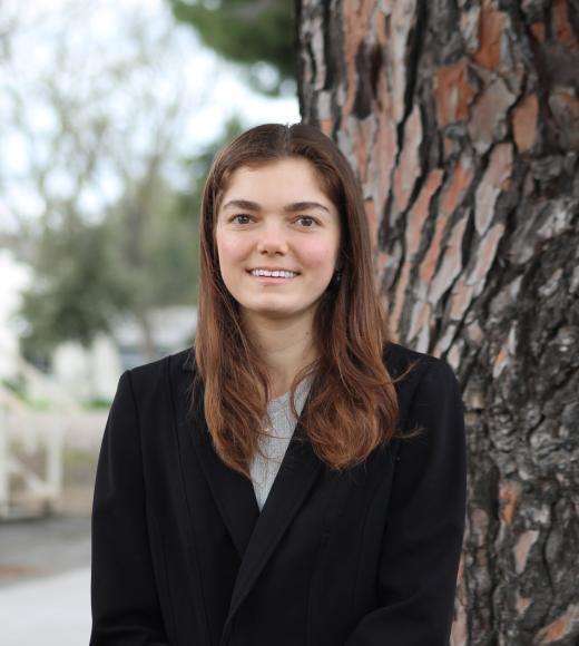 Young woman in a black sweater stands by a tree, looking joyful.