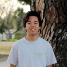 Joyful and smiling man, white T-shirt, standing by a tree.