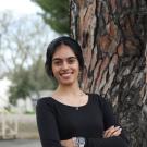 Young woman in a black sweater stands by a tree, looking joyful.