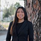 Young woman in a black sweater stands by a tree, looking joyful.